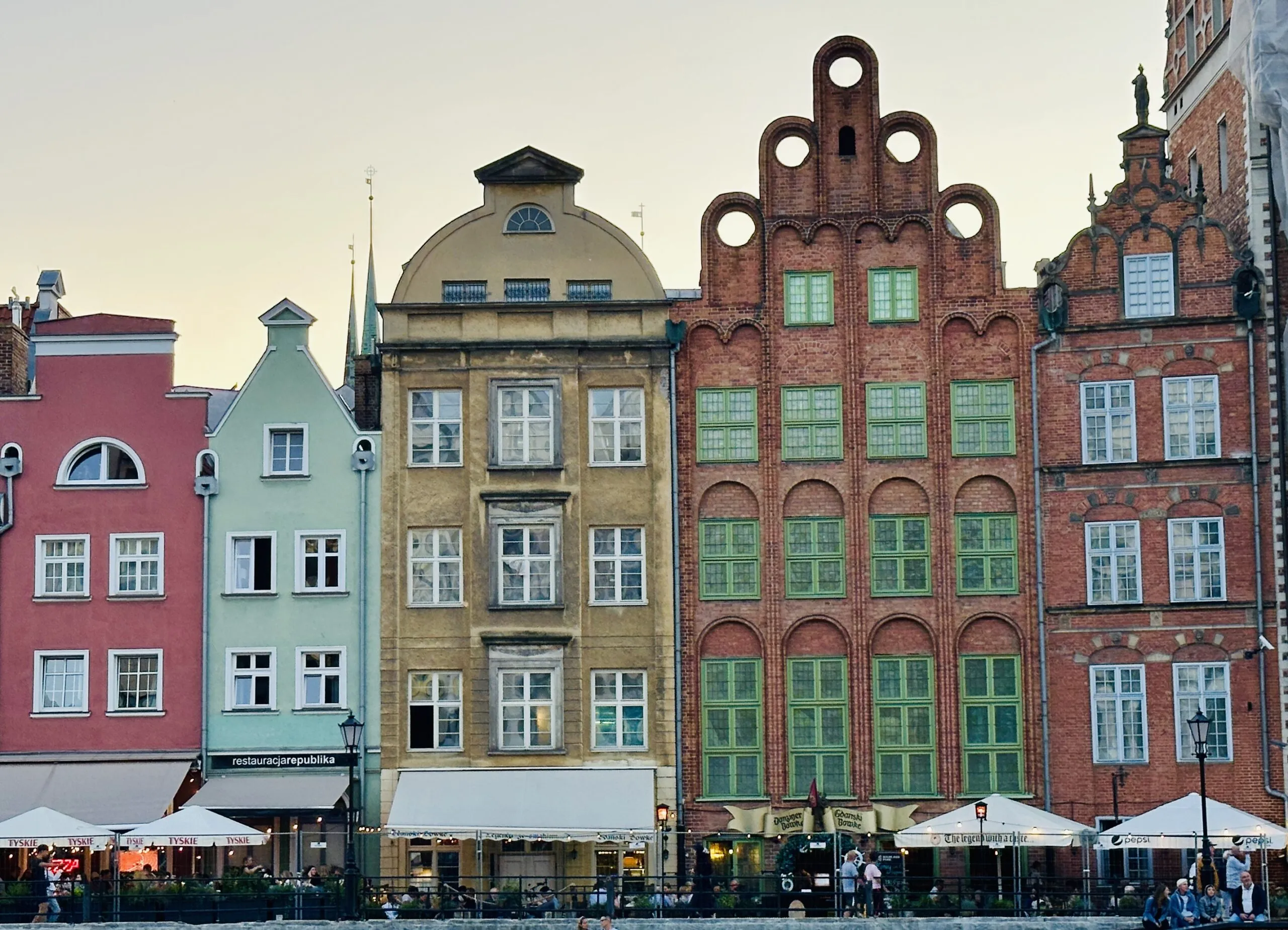 Tall gabled merchant houses along Długi Targ at dusk, painted pink, mint, ochre and brick red