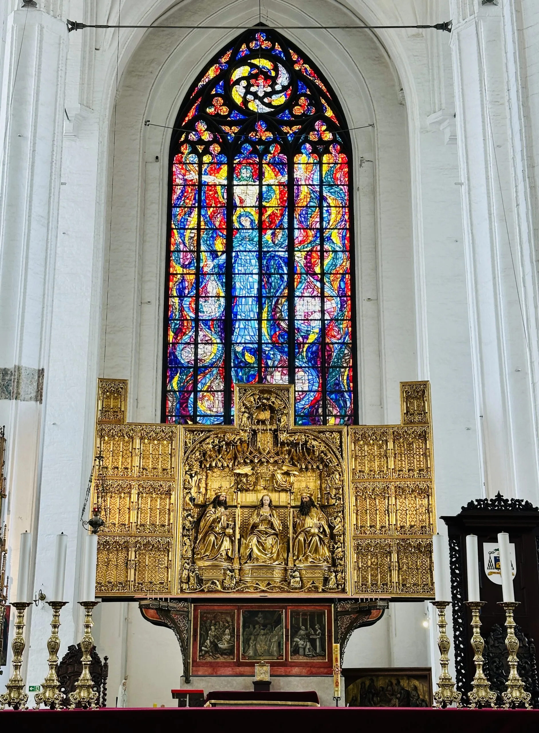 Inside St Mary's Church: a gilded carved altarpiece beneath a tall stained glass window in vivid blue, red and yellow