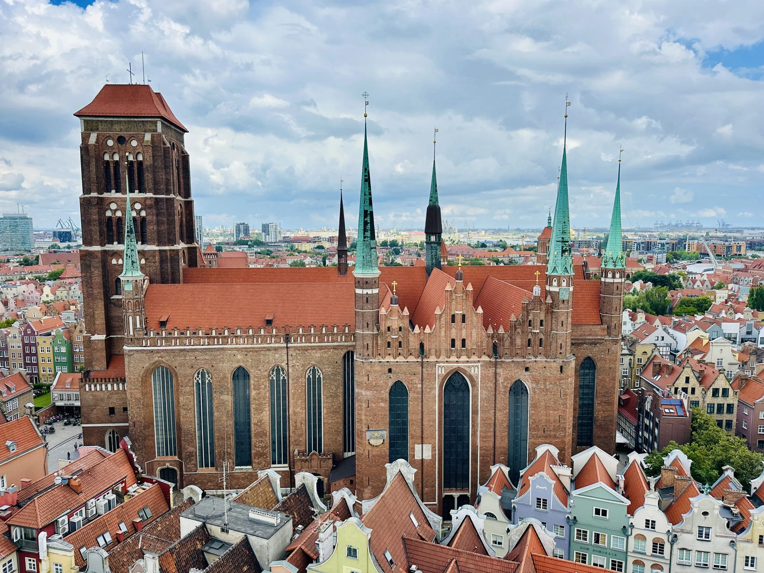 An aerial view of St Mary's Basilica, its vast red-tiled roof and brick tower surrounded by the green spires and gabled roofs of the old town