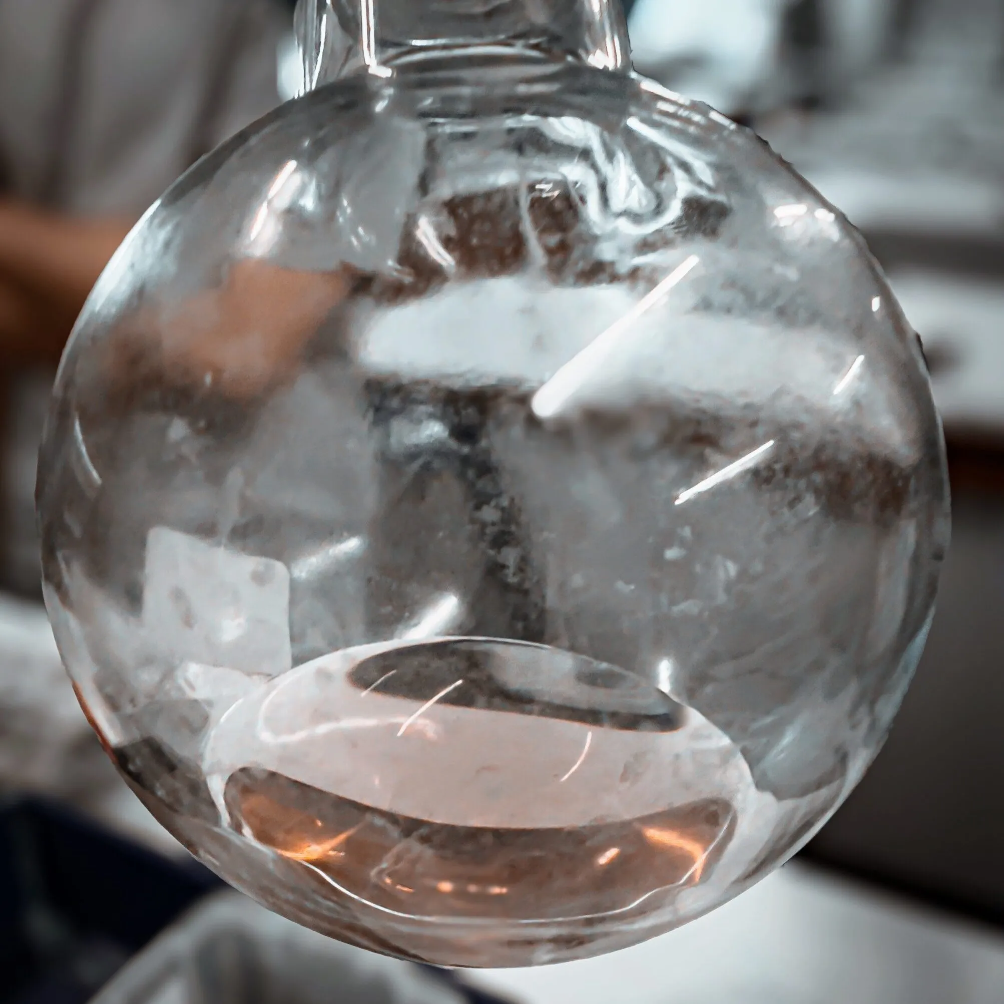 A round-bottomed flask in the lab holding a shallow layer of clear, faintly pink liquid