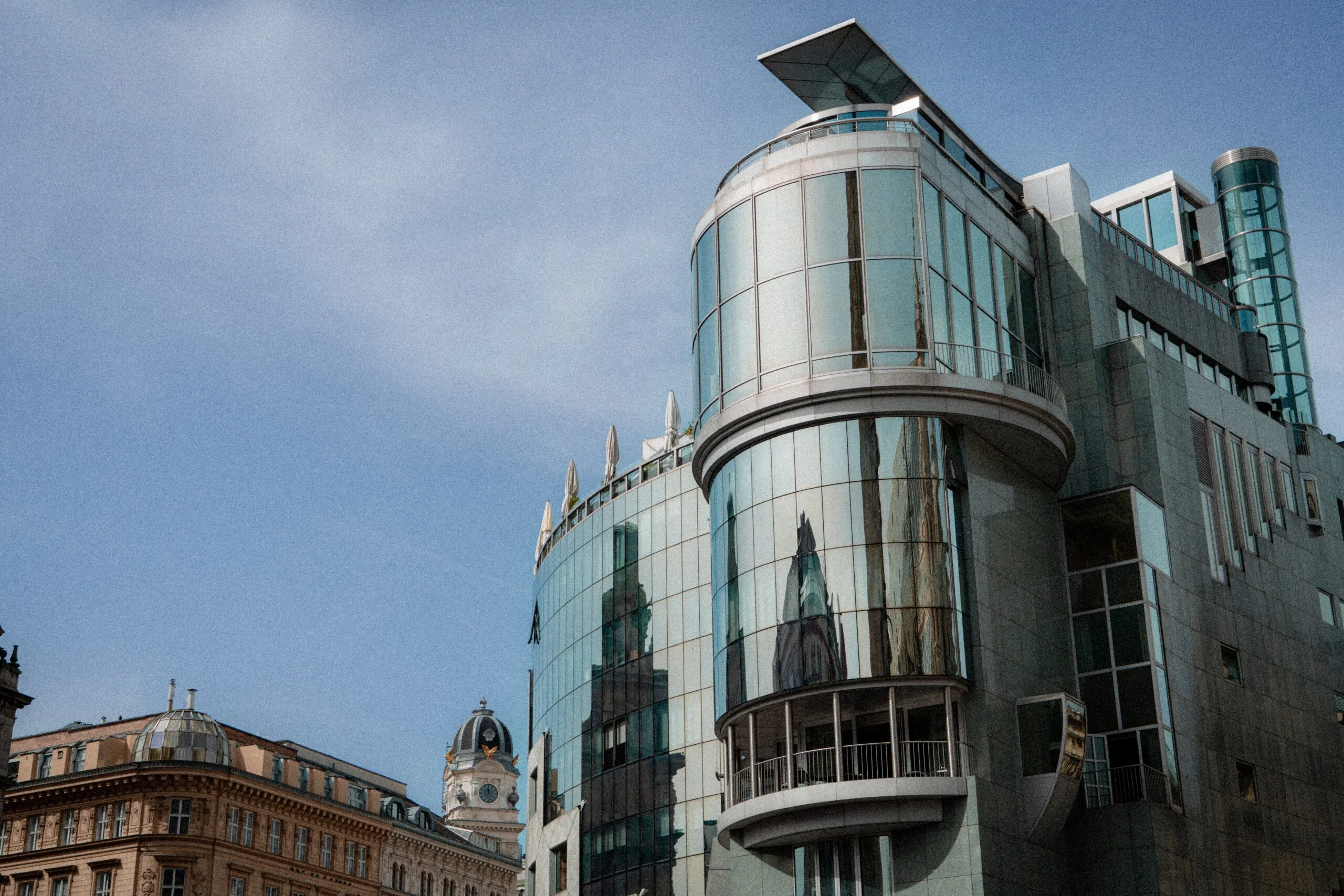 The curved glass and steel facade of the Haas House reflecting the older buildings of Stephansplatz