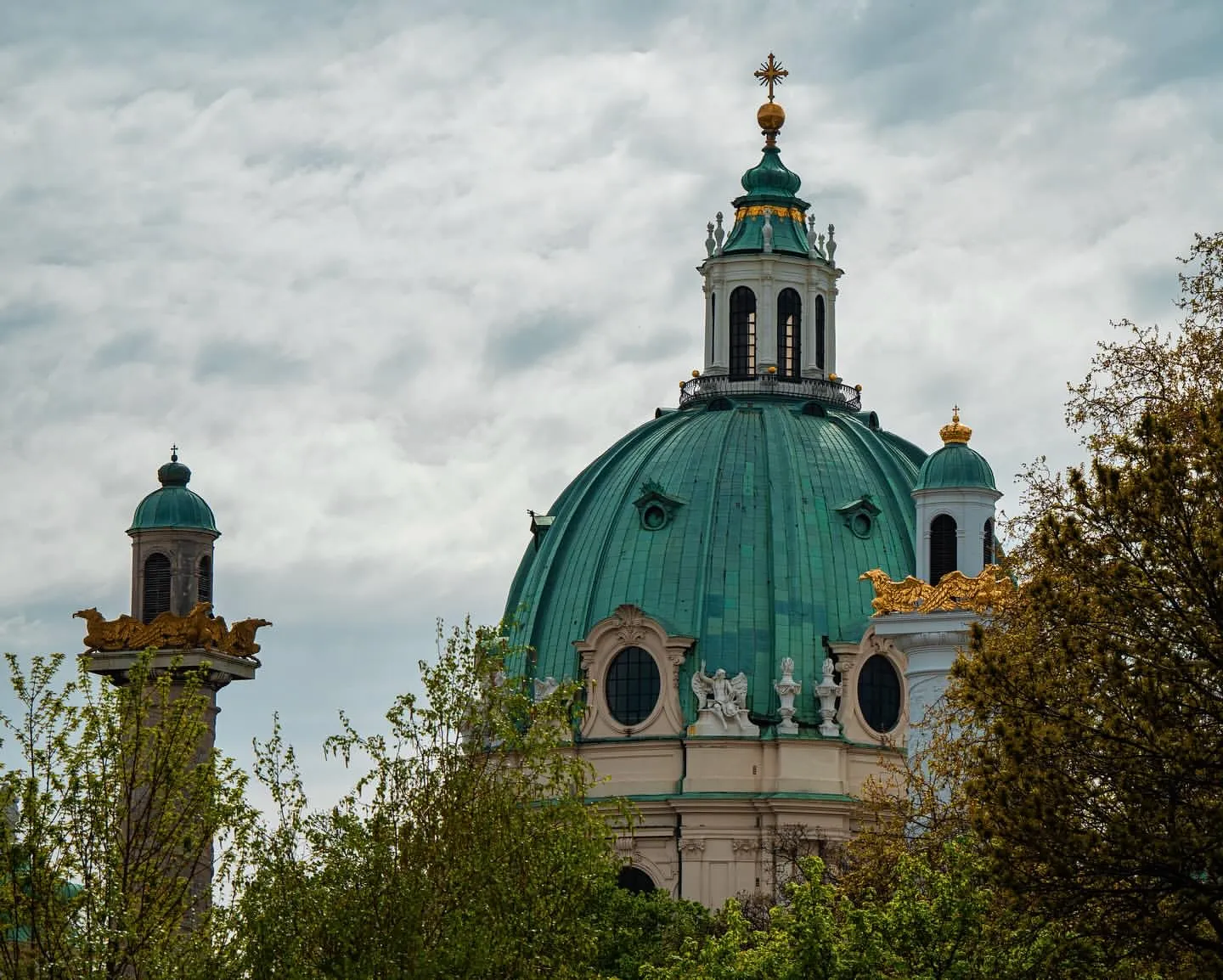 The green copper dome of the Karlskirche rising above trees, flanked by a gold-crowned triumphal column