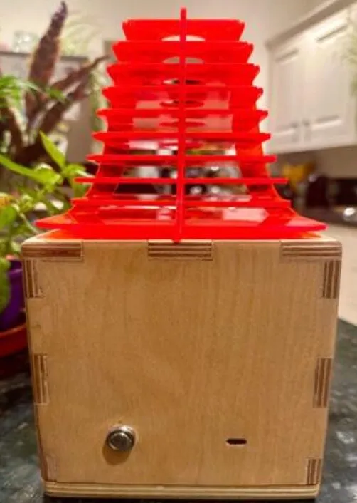 The lamp seen from the front, the plywood body's push switch and charging slot visible below the red shade