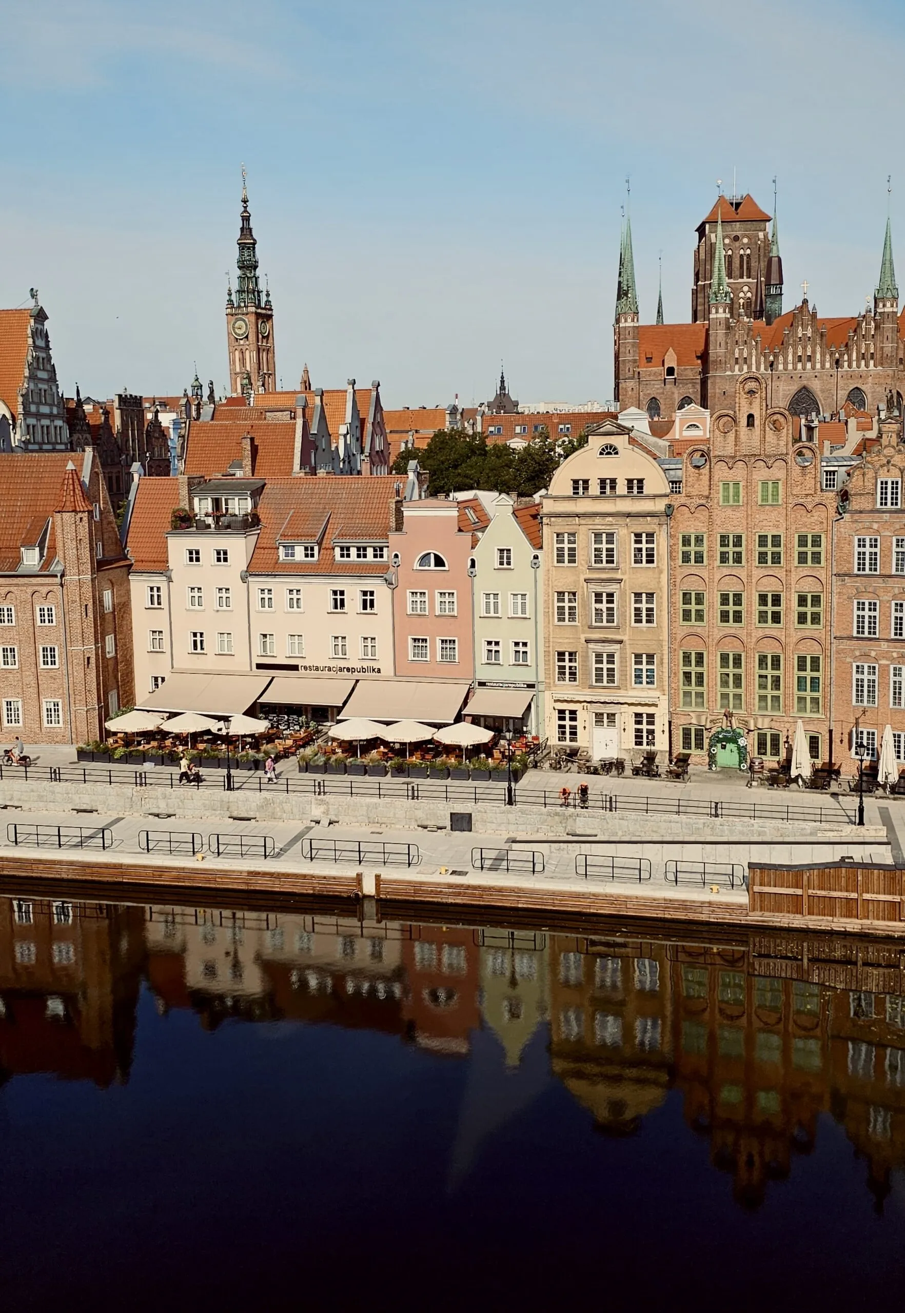 The Długie Pobrzeże waterfront in morning light, the Town Hall tower and St Mary's spires behind, all mirrored in still water